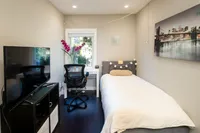 Cozy bedroom with stylish decor featuring a comfortable bed, modern desk, and vibrant artwork, illuminated by soft natural light.