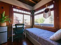Charming bedroom with large windows offering natural light, a cozy bed, and a workspace with a serene view.