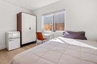 Bright and cozy bedroom with contemporary decor, featuring a comfortable bed, sleek wardrobe, and a stylish mini-fridge under natural light.