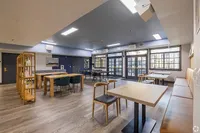 Modern communal dining area with stylish furnishings, hardwood flooring, and large windows for natural lighting.