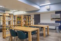 Modern communal space with stylish wooden furniture, vibrant green chairs, and a foosball table, perfect for relaxation and socializing.