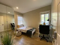 Cozy bedroom with modern decor, featuring a comfortable bed, stylish desk with chair, and ample natural light from large window.
