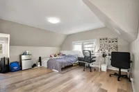 Bright and spacious bedroom with modern furnishings, featuring large windows, wooden floors, and a cozy workspace.