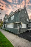 Charming multi-story home with vintage architecture, featuring rustic gray siding and nestled in a picturesque neighborhood under a vibrant sunset sky.
