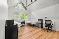 Bright and airy dorm-style room with high ceilings, featuring two single beds, cozy workstations, and modern appliances against a backdrop of lush greenery visible through large windows.