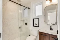 Sleek modern bathroom featuring marble walls, glass shower door, elegant mirror, and stylish fixtures.