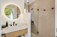Luxurious bathroom featuring a modern glass-enclosed shower, elegant herringbone tile, and a sleek vanity with stylish fixtures.