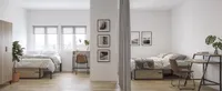 Modern apartment with two elegant bedrooms, featuring natural light, stylish wooden furniture, and lush green plants.