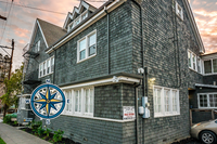 Charming grey shingle-style apartment building with classic windows, nestled on a scenic street corner at dusk.