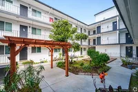 Charming apartment courtyard with lush greenery and a wooden pergola, showcasing a peaceful community atmosphere.