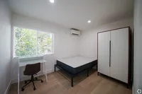 Bright and cozy bedroom featuring a spacious wardrobe, elegant desk, and large window with scenic greenery views.