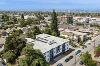 Aerial view of a vibrant neighborhood showcasing a charming apartment building surrounded by lush greenery and cityscape in the background, offering an ideal urban living experience.