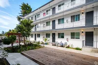 Charming apartment complex exterior featuring three levels of modern living spaces with balconies, lush landscaping, and a cozy courtyard area.