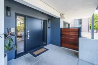 Modern apartment entrance featuring sleek black doors, elegant wood accents, and a welcoming doormat, set within a bright and airy outdoor space.
