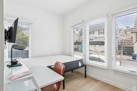 Bright and airy bedroom featuring large windows with blinds, a cozy workspace, and a mounted TV, perfect for comfort and convenience.