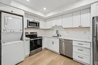 Modern kitchen with sleek stainless steel appliances, stackable washer and dryer, and elegant white cabinetry.