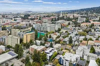 Vibrant aerial view of a bustling cityscape with diverse architecture, lush greenery, and a backdrop of rolling hills and blue skies.