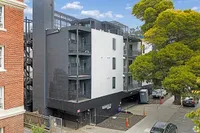 Modern apartment building with sleek black and white exterior, featuring private balconies and surrounded by lush greenery.