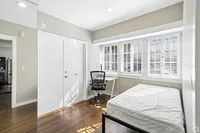 Bright, modern bedroom with floor-to-ceiling windows, a sleek desk, and hardwood floors, perfect for cozy living.