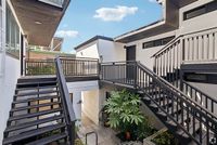 Charming apartment exterior with modern black railings and lush greenery, offering easy access through stylish staircases under a bright blue sky.