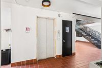 Modern apartment hallway with clean design featuring elevator access and a stylish staircase with sleek railings.