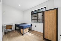 Bright and modern bedroom featuring large window, sleek wood flooring, and a cozy workspace corner.