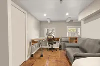 Cozy apartment corner featuring a stylish desk, modern chair, and comfy gray sofa, illuminated by recessed lighting, perfect for work and relaxation.