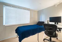Cozy bedroom with a modern single bed, study desk with computer, and bright window with blinds.