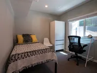 Cozy bedroom featuring a single bed with decorative pillows, a minimalist wardrobe, and a chic desk area next to a window for natural light.