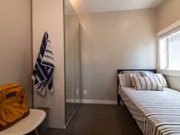 Cozy bedroom with a bed, large mirror closet, and natural light from a window, featuring a modern and minimalist design.