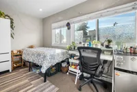 Bright and cozy bedroom with large windows, comfortable bed, and functional desk, perfect for relaxation and productivity.