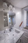 Elegant bathroom with marble countertop, modern fixtures, and ample lighting leading to carpeted hallway.