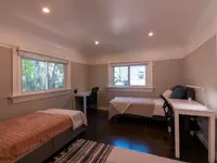 Inviting bedroom featuring two cozy beds, abundant natural light from large windows, and modern study desks for an ideal living space.