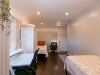 Bright and cozy bedroom featuring two single beds, a modern workspace with a sleek desk and office chair, illuminated by recessed lighting and accented with a lush indoor plant.