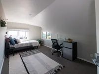 Cozy bedroom with a sloped ceiling featuring a single bed, stylish desk setup, and large windows offering natural light.