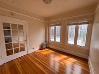 Bright, sunlit room with large windows and elegant hardwood floors, featuring a classic glass-paneled door.