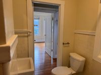Bathroom with classic tilework and polished hardwood floors, leading into a sunlit room with large windows.