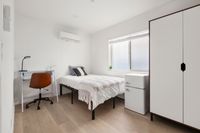 Bright and cozy bedroom featuring a single bed, sleek white wardrobe, modern desk with a stylish chair, and natural light streaming through a large window.