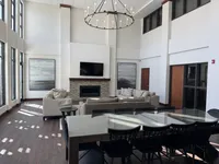 Spacious modern community room with high ceilings, elegant chandelier, and cozy fireplace, perfect for relaxation and entertaining.