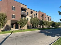 Modern apartment complex with stylish brick facade, featuring charming balconies and surrounded by lush trees on a sunny day.