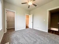Bright bedroom showcasing plush carpeting, ceiling fan, walk-in closet, and ensuite bath.