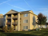 Charming apartment building with private balconies, surrounded by lush greenery and bathed in warm sunlight.