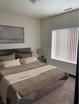 Cozy bedroom with a plush bed, soft beige tones, elegant artwork, and abundant natural light through vertical blinds.