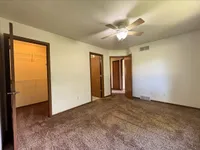 Bright bedroom with plush carpet, ceiling fan, and two doors leading to spacious walk-in closets.
