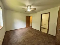 Inviting and spacious bedroom with plush carpeting, ceiling fan, and en-suite bathroom, filled with natural light from a large window.