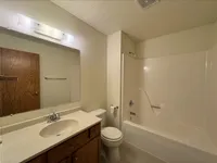 Inviting bathroom featuring a sleek vanity with wood cabinetry, large mirror, and a pristine bathtub shower combo.