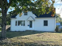 Charming single-story white house with a welcoming entrance and spacious front yard, surrounded by lush greenery and mature trees.