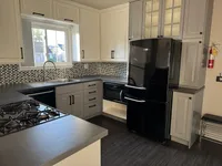 Modern kitchen with sleek black appliances, elegant white cabinets, and stylish mosaic backsplash, perfect for gourmet cooking in a cozy space.