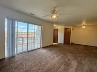 Bright and airy living room with plush carpet and large sliding glass doors opening to a private balcony, perfect for relaxation.