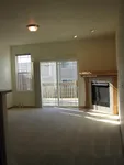 Bright living room with plush carpet, inviting fireplace, and large windows leading to a sunlit balcony.